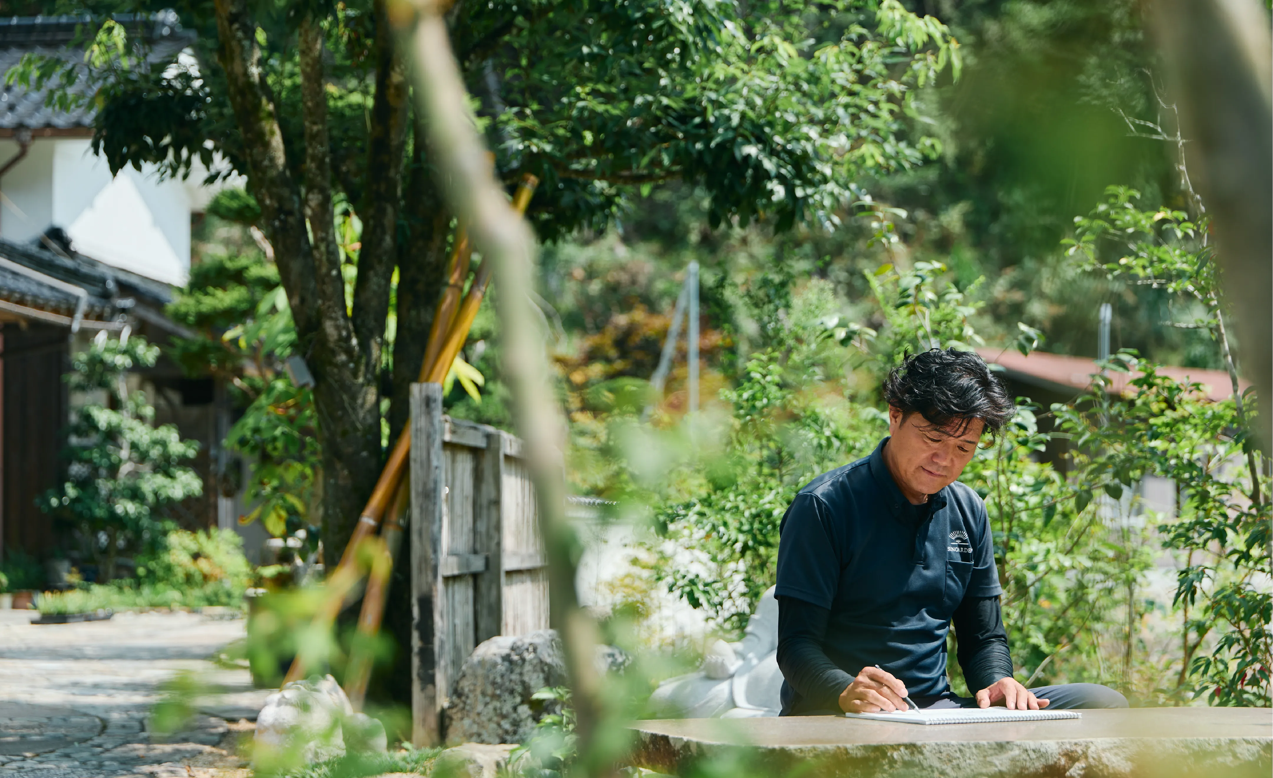 庭で紙に何かを書く男性の様子